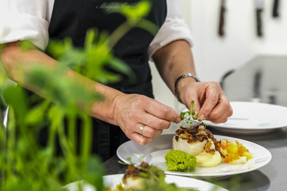 Kokk anretter klippfiskrett på kjøkken på Håholmen